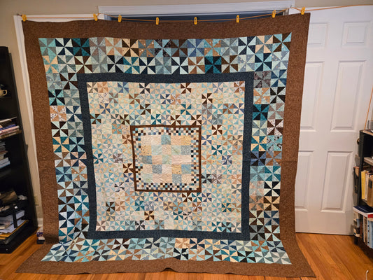 photo of entire quilt.  Blue, brown,black and biege.  Has a several borders and different scales of blocks.