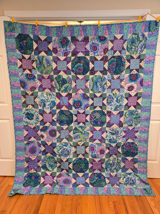 Photo of the whole quilt of blue and purple Kaffe Fassett fabrics.  Made of snowball and star blocks, looks like crosses with striped border.